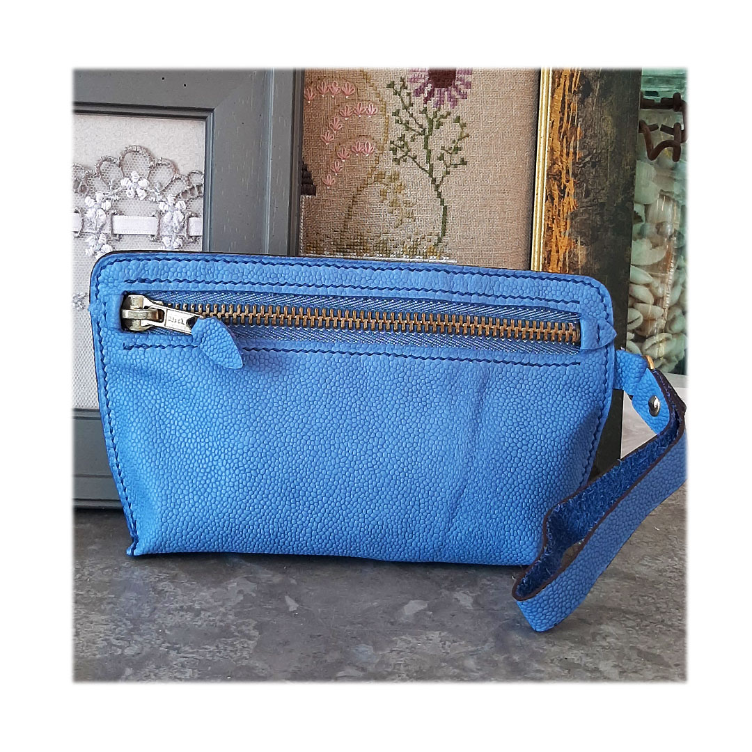 Trousse florentine. Cuir bleu avec grain caviar. Fermeture à glissière métallique. Dragonne pour l'emmener partout. Couture main point sellier au fil de lin bleu.