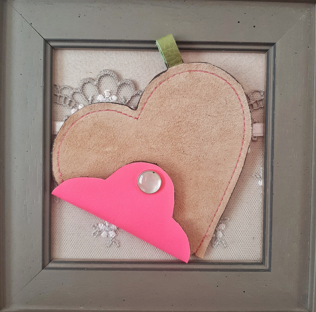 Ce porte-monnaie cœur est réalisé avec un cuir nubuck très doux au toucher dans une couleur beige. Le rabat est en cuir fluo rose, et se ferme par un bouton pression nacré.