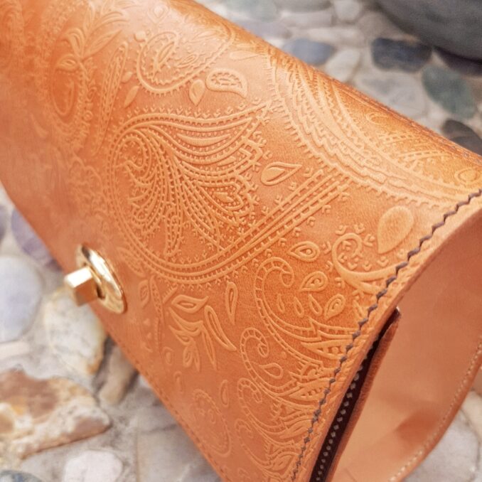 Gros plan du motif du rabat du sac qui est en cuir naturel tannage végétal. Motif cachemire gaufré. Couture du bord cousu main au fil de lin marron.