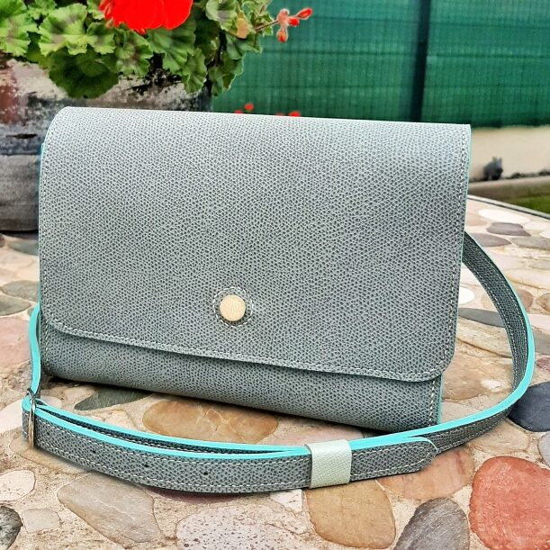 Sac d'inspiration des cartouchière. Cuir veaux Epsom bleu jean. Sur le rabat, petit bouton en nacre gravé. Couture machine, finition main. Bandoulière en cuir veaux Epsom, avec passant en cuir de chèvre type peau de chagrin bleu lagon pâle.