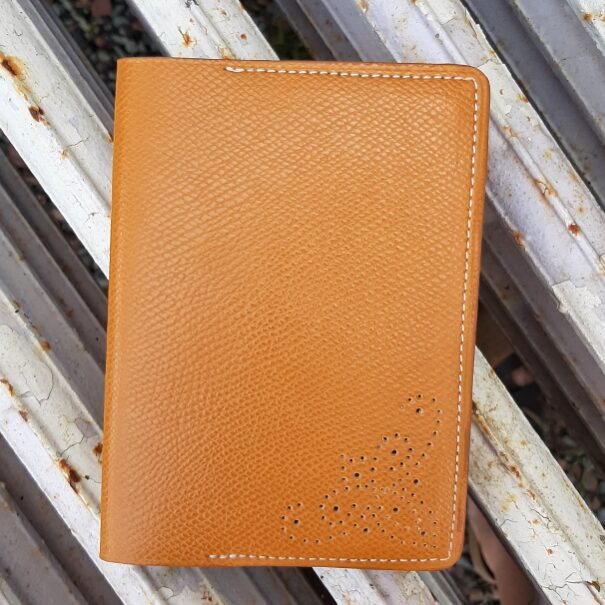 Porte passeport en cuir veaux Epsom de couleur caramel légèrement brillant. Couture machine blanc cassé, finition main. Motif ajouré bas droite du porte passeport, réalisé à la main.