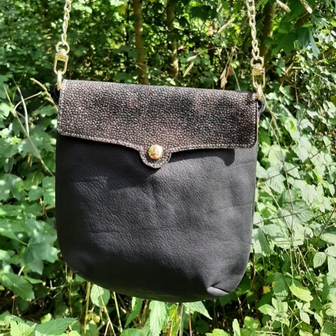 Sac bandoulière de la collection Myrlande. Cuir pleine fleur couleur noir et rabat grain imitation galuchat noir aux reflets dorés. Bouton doré magnétique. Couture main au point sellier. Bandoulière amovible moitié chaîne métal doré avec mousquetons, cuir noir