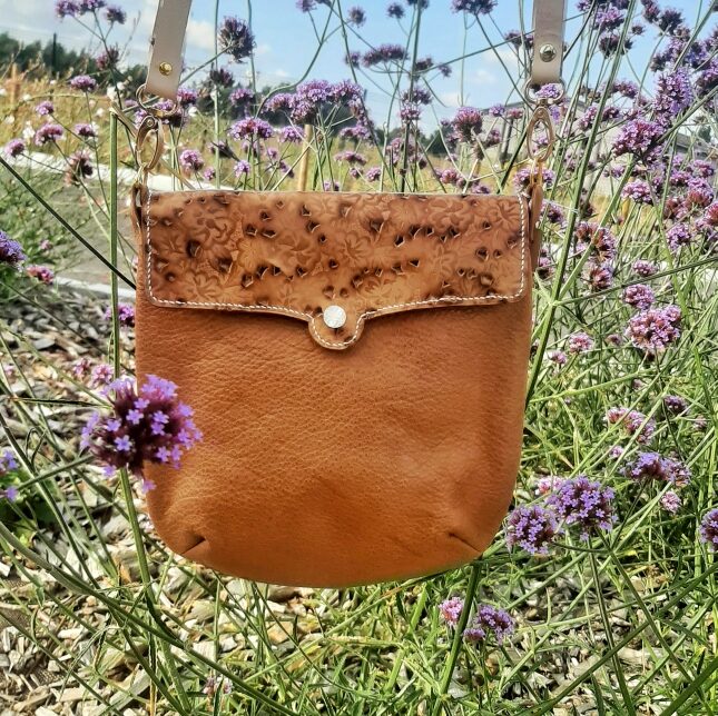 Sac bandoulière de la collection Myrlande. Cuir pleine fleur couleur caramel. Rabat cuir naturel tannage végétal motif floraux gaufré et perforé dessus. Bouton nacre gravé sur le rabat et magnétique. Couture main au point sellier. Bandoulière réglable et amovible grâce à ses mousquetons en cuir naturel tannage végétal. Couture main au point sellier avec fil de lin blanc cassé.