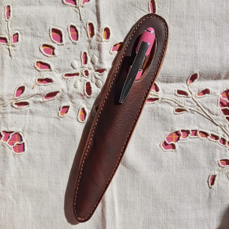 Étui à stylo minimaliste sur mesure en cuir marron pull-up, cousu main au fil de lin, avec finition des tranches ocre, contenant un stylo à clip métallique.