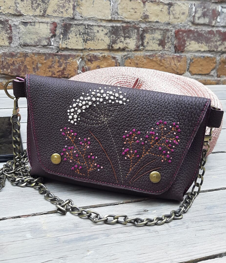 Petit sac en cuir grainé bordeaux avec rabat brodé main en broderie cannetille florale, intérieur en agneau rose foncé, bandoulière en chaîne, fabrication artisanale française.