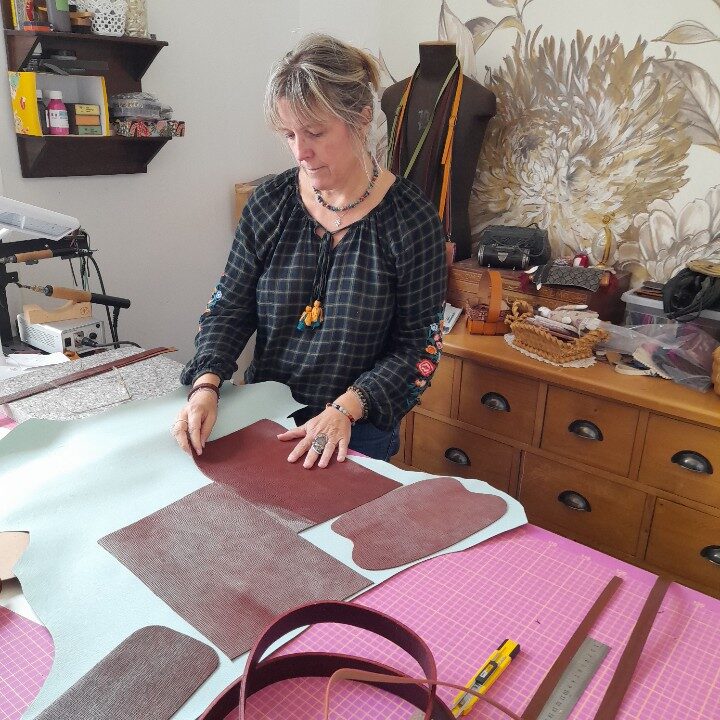 Vous me voyez dans mon atelier en train de placer des pièces de cuir découpées sur la table.