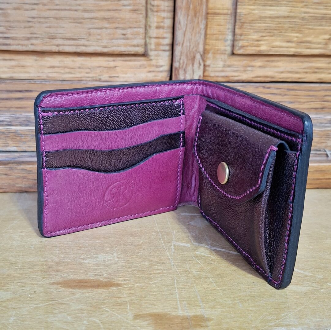 Portefeuille de couleur prune, violet en cuir tannage végétal, position ouverte où l'on voit à droite le compartiment pour la monnaie, et à gauche compartiment pour loger 3 cartes. Cousu main au point sellier.
