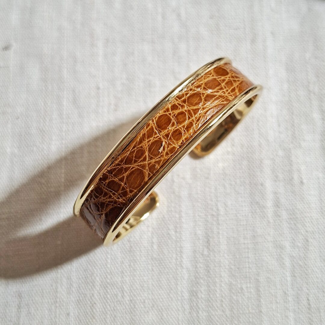 bracelet manchette en métal doré clair et cuir d'alligator marron avec un vernis brillant. Le bracelet est réglable à votre poignet