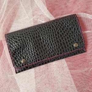 Compagnon en cuir vernis noir, gaufrage imitation crocodile. Deux boutons pressions métalliques argenté sur le rabat permettent de bien fermer cette pochette compagnon. Couture main au point sellier au fil de lin couleur fuchsia.