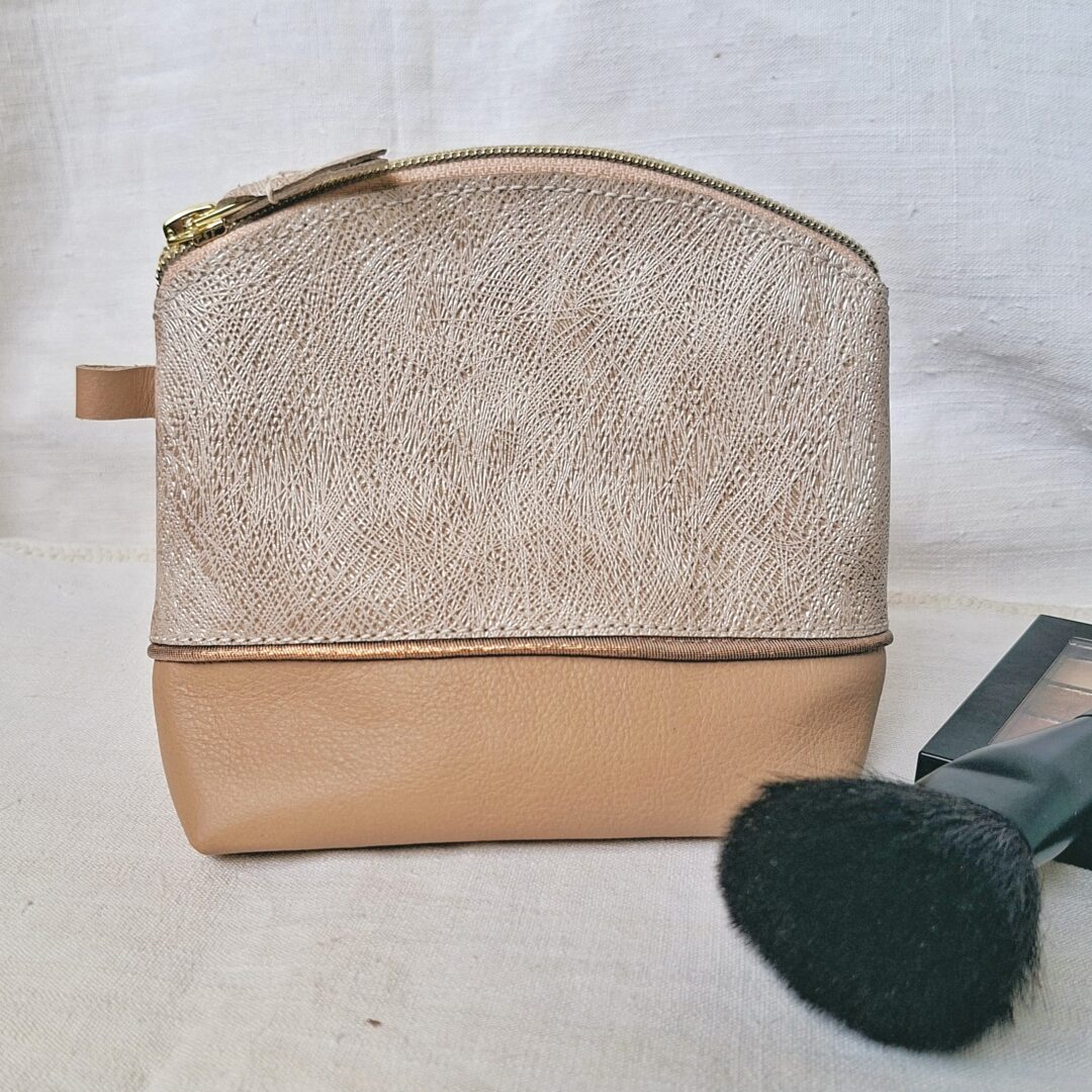 Trousse en cuir de chèvre fantaisie, avec des motifs embossés de traits et brillant sur un fond crème. le bas de la troussé est en cuir de bovin de couleur beige. Un biais doré sépare les 2 cuirs. Fermeture à glissière assorti au cuir.