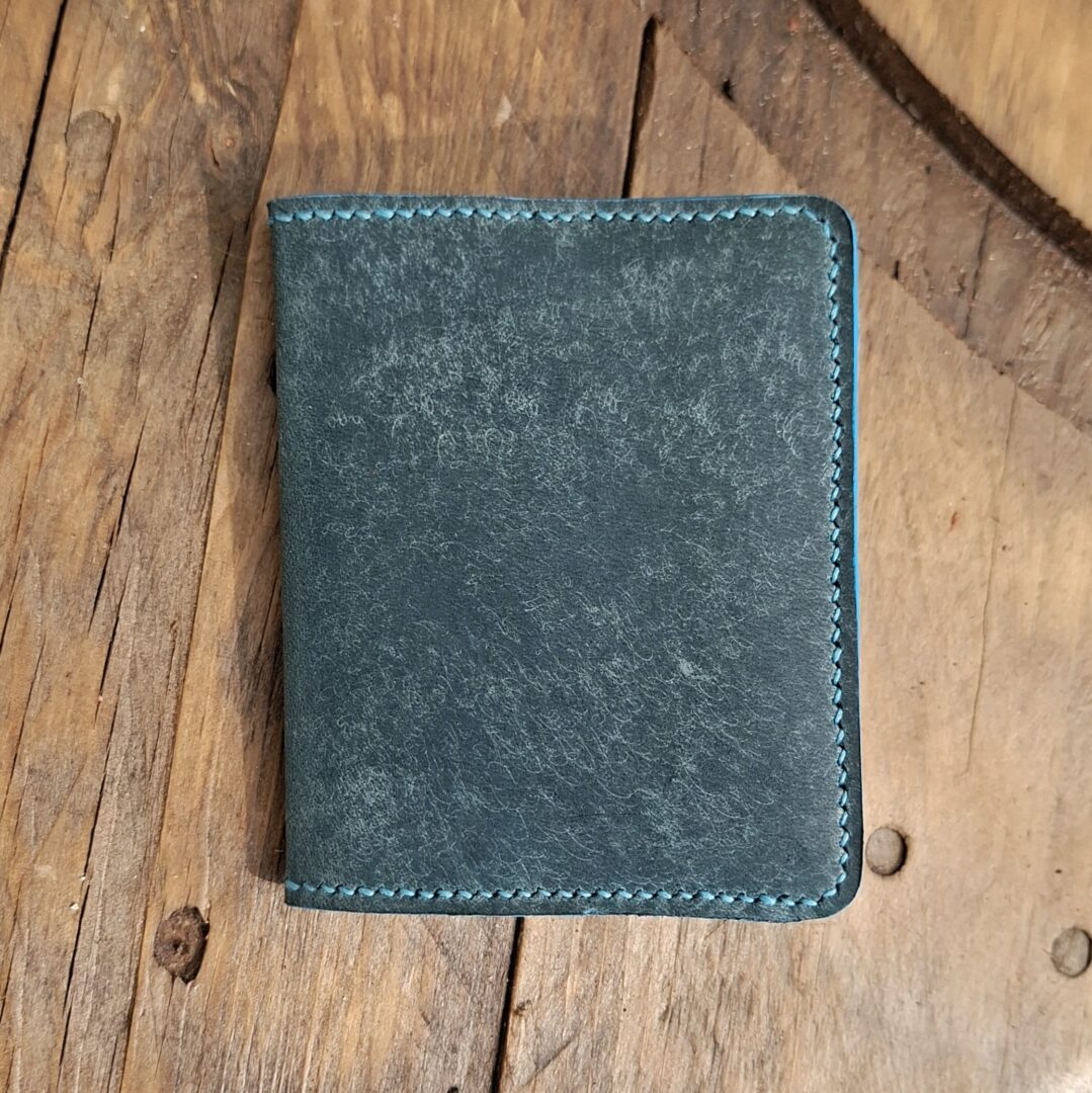 Porte-cartes en cuir bleu turquoise foncé fermé sur table en bois