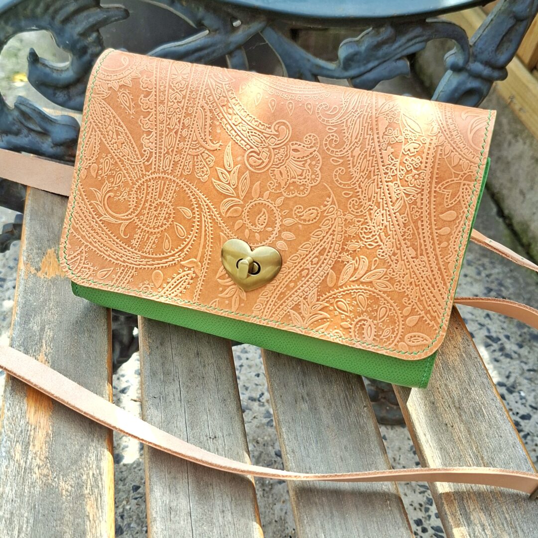 Sac artisanal en cuir embossé posé sur une chaise en bois, détails du motif cachemire et fermoir cœur vintage.