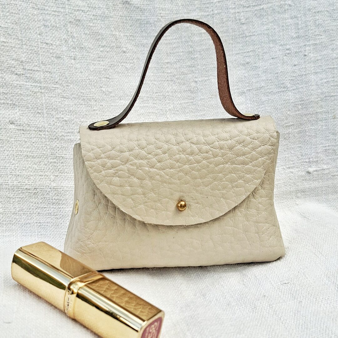 Petit sac en cuir pleine fleur grain de café blanc cassé fabriqué à la main, avec poignée en cuir pleine fleur marron et fermeture par bouton de col.