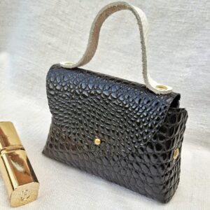 Petit sac en cuir de chèvre verni noir imitation crocodile, fabriqué à la main avec poignée en cuir pleine fleur blanc cassé et fermeture par bouton de col.