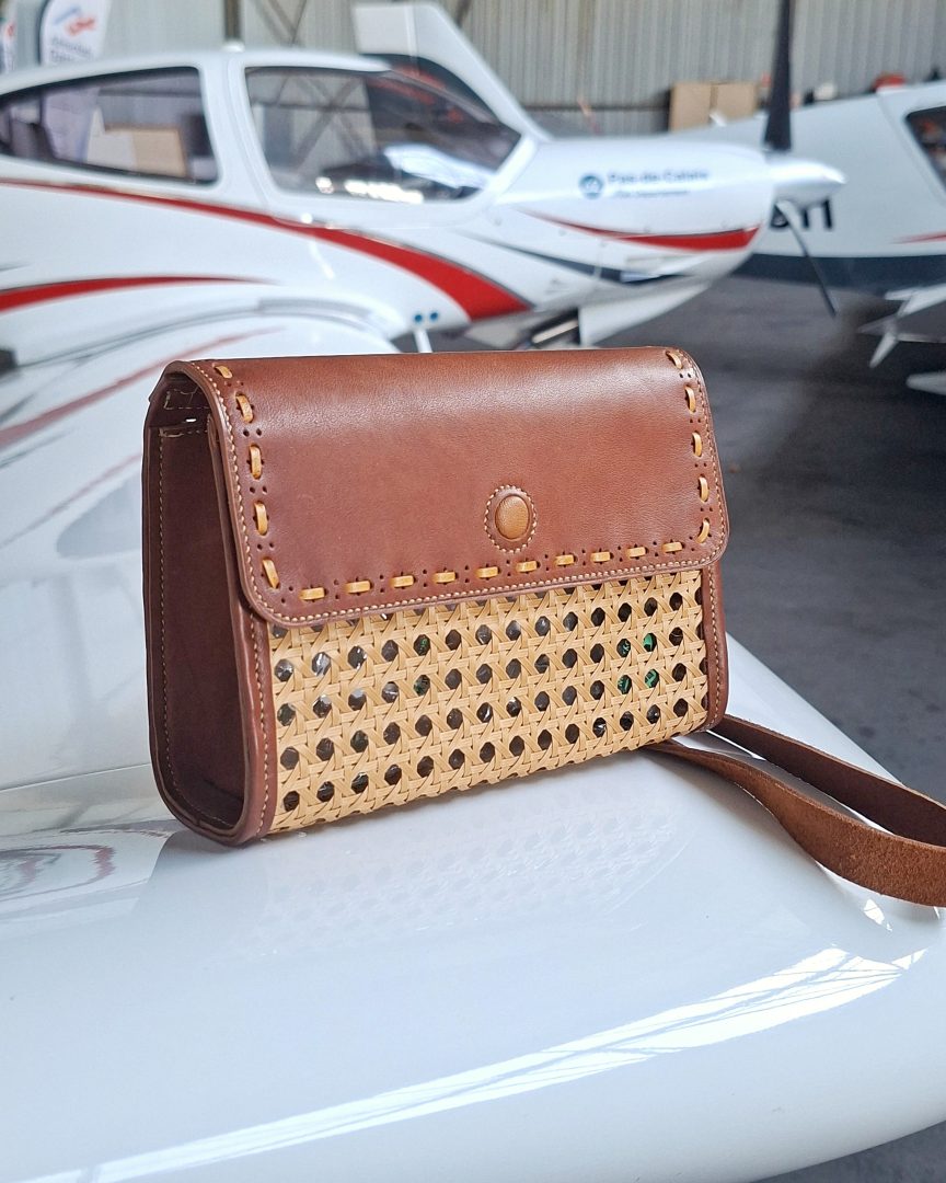 Sac cartouchière en cuir cognac et osier tressé photographié sur un avion, création artisanale française